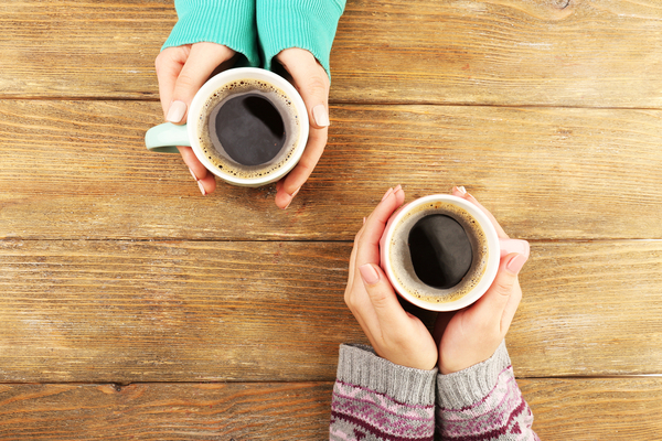 Hands of two ladies holding a cup of coffee