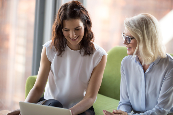 Two women sitting on a couch while talking and looking at the laptop