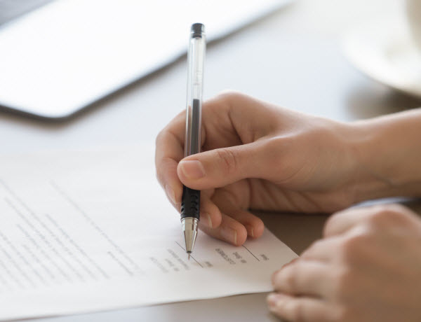 female hand holding pen, putting signature on legal document