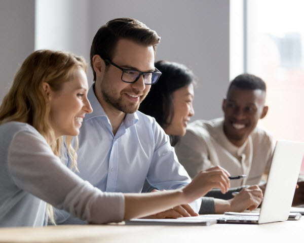 Happy young female employee discussing online project, showing computer presentation to skilled team leader in eyeglasses